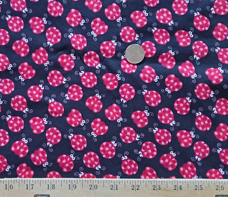 May include: Black fabric with a repeating pattern of red ladybugs. The ladybugs have white spots and are outlined in white.