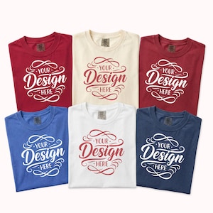 May include: Six t-shirts in various colors: red, cream, white, blue, and navy. Each shirt features the text "YOUR DESIGN HERE" in a decorative script. The shirts are arranged on a white background.
