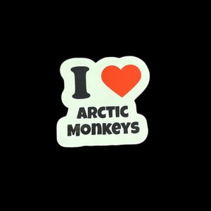 Puede incluir: Una pegatina con el texto "I ♥ ARCTIC MONKEYS". La "I" es negra, el corazón es rojo y el texto es en negrita y sin serifa. La pegatina tiene un fondo blanco y un borde negro, sobre un fondo negro.