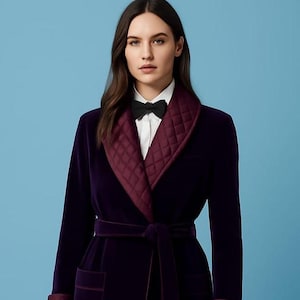May include: A luxurious, dark purple velvet robe with a quilted burgundy collar and cuffs. The robe features a matching belt and a white shirt with a black bow tie. The background is a solid light blue.