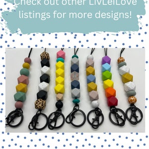 May include: Seven colorful silicone bead keychains with different patterns and colors. Each keychain has a black metal lobster clasp and a black metal ring. The keychains are arranged in a row on a white surface. Check out other LivLeiLove listings for more designs!