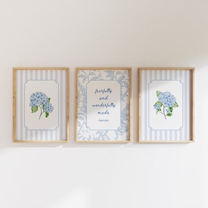 May include: Three framed wall art prints with light wood frames. The two outer prints feature blue hydrangea illustrations on a light blue and white striped background. The center print displays the text fearfully and wonderfully made Psalm 139:14.