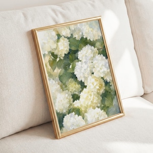 May include: A rectangular wall art print in a thin gold frame featuring a watercolor painting of white and pale yellow hydrangea flowers with deep green leaves. The artwork displays soft, blended brushstrokes and a light, airy color palette.