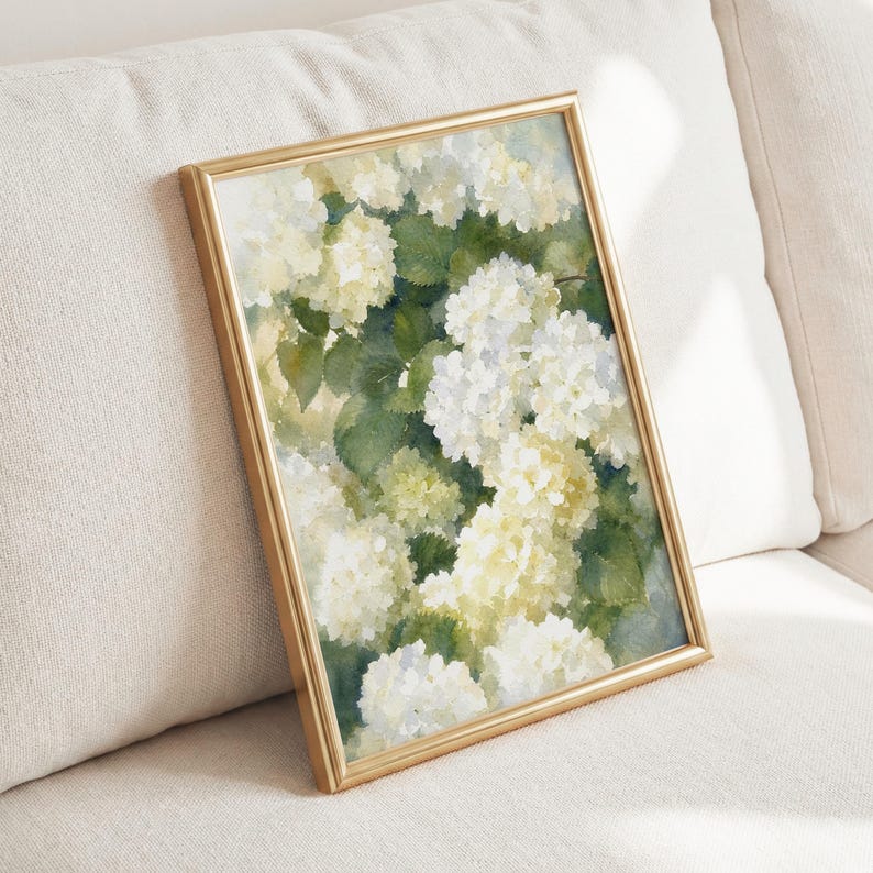 May include: A rectangular wall art print in a thin gold frame featuring a watercolor painting of white and pale yellow hydrangea flowers with deep green leaves. The artwork displays soft, blended brushstrokes and a light, airy color palette.
