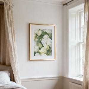 May include: A rectangular wall art print featuring a watercolor painting of white and pale yellow hydrangea flowers with green foliage, encased in a thin metallic gold frame with a wide white mat border, displayed on a plain white wall.
