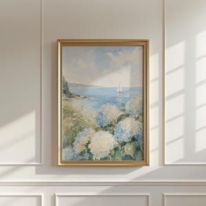 Op de afbeelding: Een ingelijste verticale wandkunstprint met een schilderij van een kustlandschap. De scène toont een kalme blauwe oceaan met een kleine witte zeilboot in de verte, een rotsachtige kustlijn met groene bomen en grote trossen blauwe en witte hortensia's.