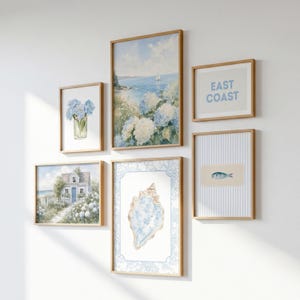 May include: A gallery wall set of six framed prints featuring coastal and floral themes. The collection includes watercolor illustrations of blue hydrangeas, a seaside cottage, a seashell, a fish, and text reading EAST COAST in blue.