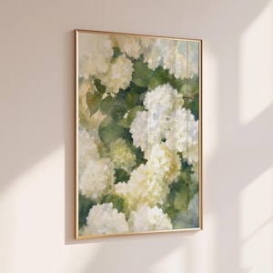 May include: A vertical rectangular wall art print in a thin gold frame featuring a watercolor painting of white and cream hydrangea flowers with green leaves. The artwork displays soft brushstrokes and a botanical theme with light tones.