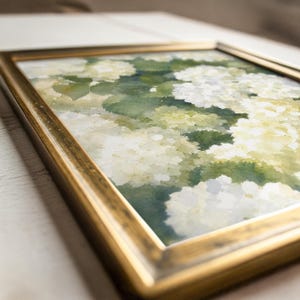 May include: A framed watercolor painting featuring clusters of white and pale green hydrangea flowers with soft, blended green foliage. The artwork is encased in a metallic gold frame with a slightly weathered finish, viewed from an angled perspective.
