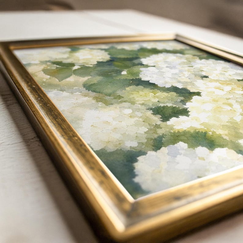 May include: A framed watercolor painting featuring clusters of white and pale green hydrangea flowers with soft, blended green foliage. The artwork is encased in a metallic gold frame with a slightly weathered finish, viewed from an angled perspective.