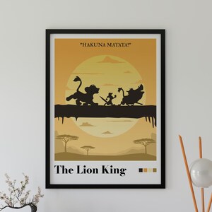 Puede incluir: Un póster enmarcado con un fondo de atardecer amarillo y naranja con siluetas negras de tres personajes caminando sobre un tronco. El texto dice "HAKUNA MATATA!" en la parte superior y "The Lion King" en la inferior, con cuatro pequeños cuadrados de color.