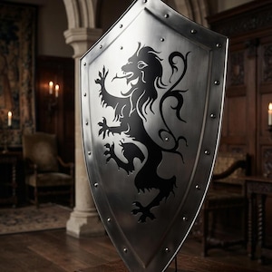 Puede incluir: Un escudo de metal plateado con la silueta de un león rampante negro en el centro. El escudo tiene una base puntiaguda, un borde reforzado y está asegurado con remaches metálicos espaciados uniformemente a lo largo del borde exterior.