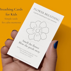 May include: A white card with the text "Breathing Cards for Kids" and "Simple tools for calm moments" on a yellow background. The card also has the text "FLOWER BREATHING" and instructions for breathing exercises. A hand holds the card.