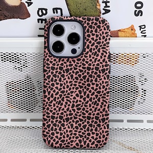 May include: A pink phone case with a black spotted pattern. The case has a camera cutout and button covers. The case is designed to fit a smartphone.