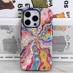 Puede incluir: Una funda de teléfono colorida con un diseño abstracto vibrante. La funda presenta un patrón arremolinado de azules, rosas, amarillos y verdes, con acentos de estrellas. La funda tiene un borde negro y un recorte para la cámara.