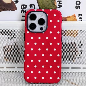 May include: A red phone case with a white polka dot pattern. The case has a black camera ring and is designed for a smartphone. The case is made of a smooth material and has a glossy finish.