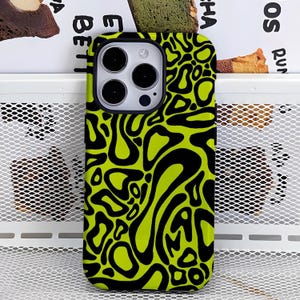May include: A phone case with a black and neon green abstract pattern. The case has a black camera lens surround and a black border. The design features organic shapes and swirls.