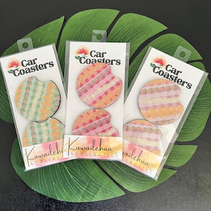 May include: Three sets of car coasters in clear packaging, each with a unique patterned design. The coasters feature a mix of colors including green, pink, and orange. The packaging includes the text "Car Coasters" and "Kawailehua & Collective".