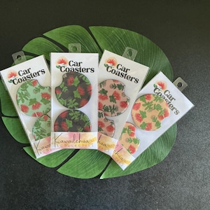 May include: Four car coaster sets with floral designs. Each set includes two coasters with a different floral pattern. The coasters are packaged in clear plastic with the words "Car Coasters" printed on the top. The background is a large green leaf.