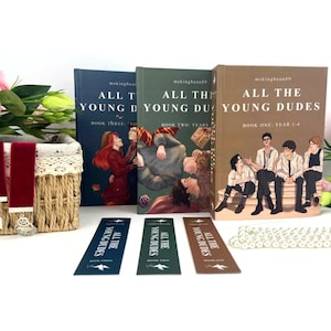 May include: Three hardcover books and matching bookmarks with the title "All The Young Dudes." The books have different colored covers with illustrations. Bookmarks are navy, green, and brown. A decorative basket and faux pearls are also in the image.