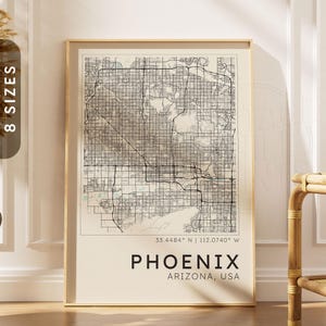 Puede incluir: Una lámina de arte mural enmarcada que muestra un mapa callejero detallado de Phoenix, Arizona, EE. UU. El mapa presenta redes de carreteras negras sobre un fondo crema con las coordenadas geográficas 33.4484 N | 112.0740 W y el texto PHOENIX ARIZONA, USA.