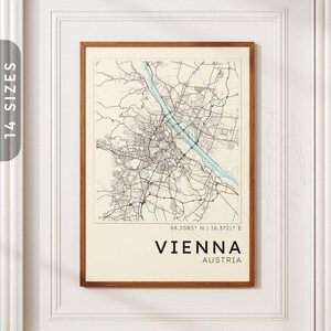 May include: A framed map print of Vienna, Austria, featuring black street lines on a cream background with a light blue river running diagonally. The text reads 48.2085 N | 16.3721 E, VIENNA, and AUSTRIA in black capital letters at the bottom.