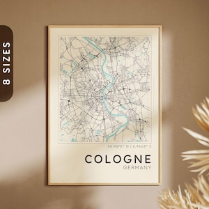 May include: A framed map print of Cologne, Germany, featuring a detailed street layout in black lines against a cream background. The Rhine River is highlighted in light blue. The city name and country are printed in black at the bottom.