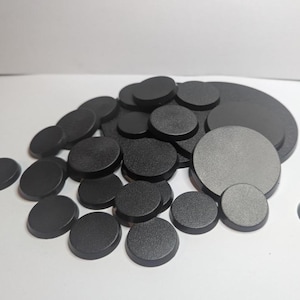 Puede incluir: Un conjunto de bases circulares negras de varios tama&ntilde;os. Las bases tienen un acabado mate y est&aacute;n dispuestas en una pila, con algunas dispersas. Las bases son probablemente para miniaturas o modelos.