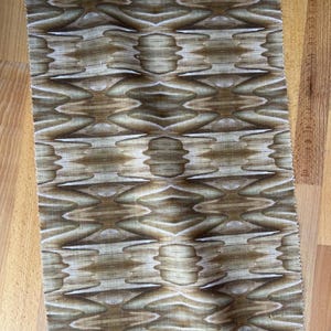 May include: A rectangular piece of fabric with a repeating pattern of brown and white organic shapes. The design resembles a stylized wood grain or a series of interconnected, symmetrical forms. The fabric has a slightly textured appearance.