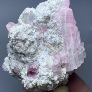 May include: A natural mineral specimen with pink tourmaline crystals set in a white, textured rock matrix. The tourmaline crystals are a vivid pink colour and have a distinct crystalline structure.