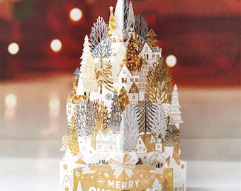 Può includere: Biglietto di Natale 3D con una scena di villaggio, realizzato con ritagli di carta dorata, argentata e bianca. Il biglietto presenta un design a strati con case, alberi e la scritta "MERRY CHRISTMAS". Una decorazione festiva.