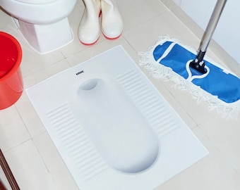Puede incluir: Un inodoro blanco de suelo con base rectangular y abertura redondeada. Un cubo rojo, botas blancas con suelas rojas y una fregona azul están cerca. El suelo es de baldosas.