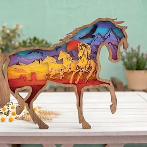 May include: A multi-layered wooden cutout in the shape of a horse, featuring a colourful landscape scene inside. The design depicts three horses running across a desert terrain with mountains, a red sun, and a bird silhouette against a purple sky.