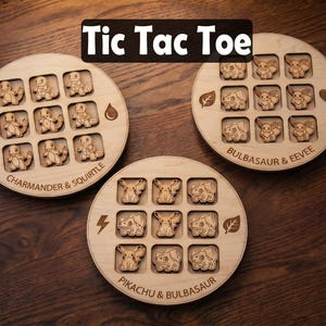 May include: Three circular wooden tic tac toe boards featuring engraved character designs. One board shows Charmander and Squirtle, another Bulbasaur and Eevee, and the third Pikachu and Bulbasaur. Each board includes elemental icons and text labels.