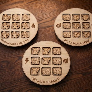 May include: Three circular light-coloured wooden tic-tac-toe boards featuring laser-engraved character designs. Each board has a 3x3 grid with wooden game pieces depicting various creatures, along with engraved text and symbols like fire, water, leaf, and heart.