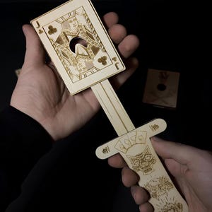 Puede incluir: Truco de cartas de madera cortada con láser con un diseño de Jota de Tréboles. El mango está decorado con símbolos de naipes y una calavera. El texto dice "Laser Cut Files" y "Tricks for kids and adults."