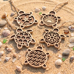 May include: Five wooden turtle ornaments with intricate cutouts, including designs of starfish, a sunrise, a geometric shell pattern, a floral mandala, and ocean waves. Each turtle features a light wood frame and a dark wood backing with a twine loop.