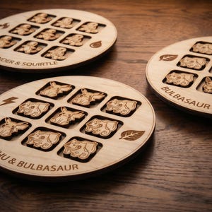 May include: Three circular light-coloured wooden game boards featuring laser-engraved character illustrations and text. The boards are labelled Charmander & Squirtle, Bulbasaur & Eevee, and Pikachu & Bulbasaur, with elemental icons like fire, water, and leaves.
