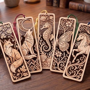 Puede incluir: Cinco marcapáginas rectangulares de madera con intrincados diseños cortados a láser de un zorro, un lobo aullando a una luna creciente, un caballito de mar, una mariposa y un caballo. Cada marcapáginas incluye una borla de tela verde, granate, dorada o azul.
