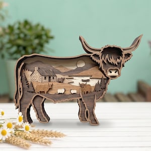 Peut inclure: Sculpture en bois représentant une vache des Highlands avec un design en couches. La sculpture présente un paysage détaillé à l'intérieur, comprenant un chalet, des arbres et d'autres animaux. La vache est brune avec de grandes cornes.