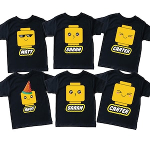 May include: Black t-shirts with yellow Lego-style character faces, each with a different expression. The shirts have names like "Matt", "Sarah", "Carter", and "Andy" printed below the faces. The shirts are for children.