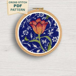 May include: A cross-stitch PDF pattern featuring a floral design. The embroidery is set in a wooden hoop, showcasing a vibrant orange and yellow flower with green leaves against a dark blue background. The text "CROSS STITCH PDF PATTERN" is visible.