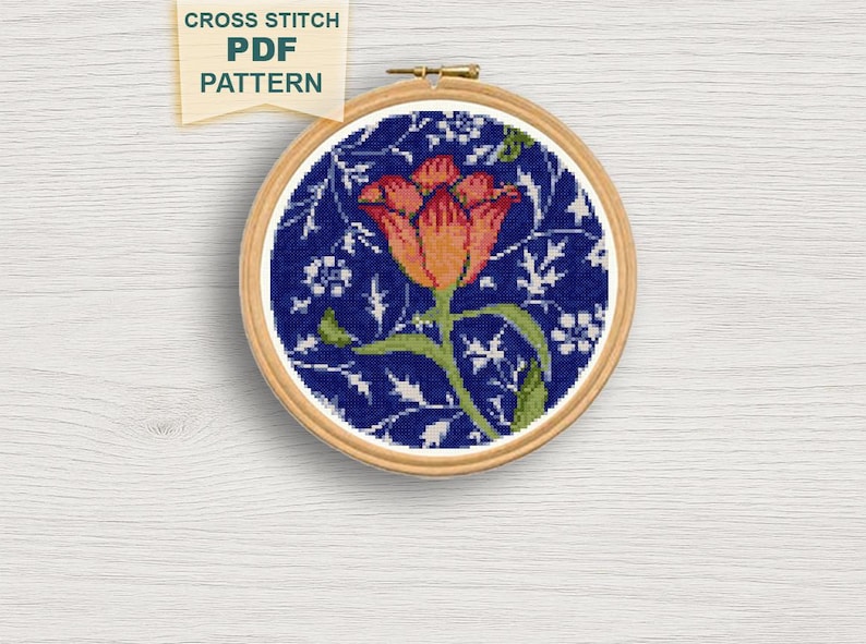 May include: A cross-stitch PDF pattern featuring a floral design. The embroidery is set in a wooden hoop, showcasing a vibrant orange and yellow flower with green leaves against a dark blue background. The text "CROSS STITCH PDF PATTERN" is visible.