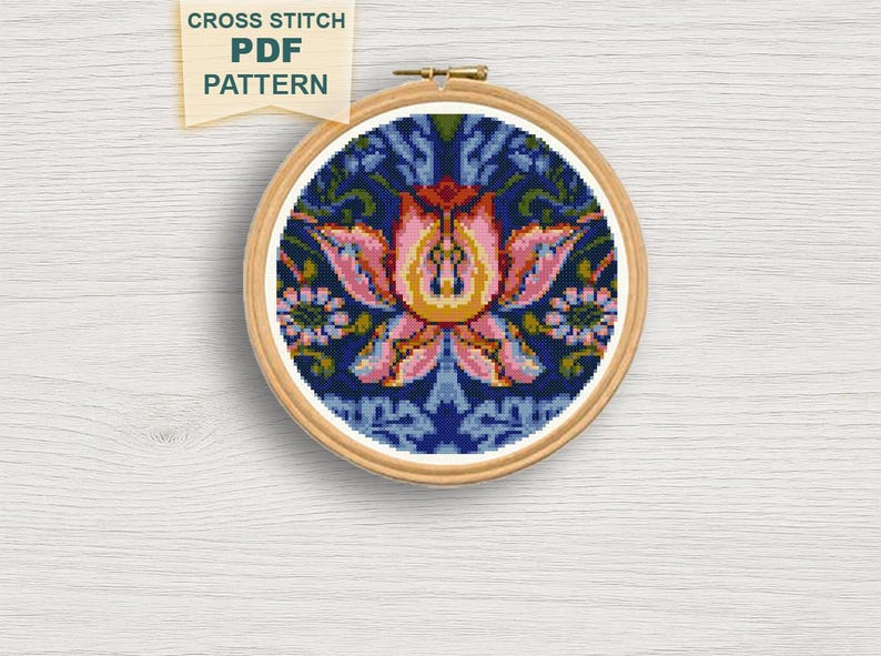 May include: A cross-stitch pattern in a wooden hoop. The design features a central pink and yellow floral motif on a dark blue background. The text "CROSS STITCH PDF PATTERN" is in a banner at the top.
