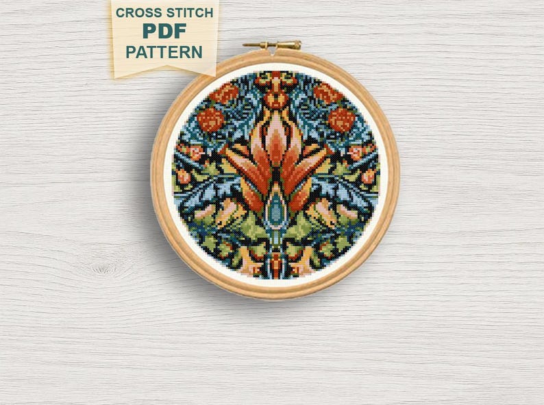 May include: A completed cross-stitch project in a wooden hoop. The design features a symmetrical floral pattern with orange, blue, green, and peach hues. The text "CROSS STITCH PDF PATTERN" is on a tan banner.