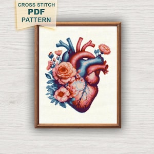 May include: A framed cross-stitch PDF pattern featuring a detailed anatomical heart design adorned with pink and blue flowers. The heart is rendered in shades of red and blue, with the text "CROSS STITCH PDF PATTERN" in a corner.