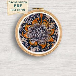 May include: A cross-stitch PDF pattern featuring a floral design in a wooden embroidery hoop. The design showcases a large, stylized flower with orange and white petals against a dark blue background. The text "CROSS STITCH PDF PATTERN" is visible.