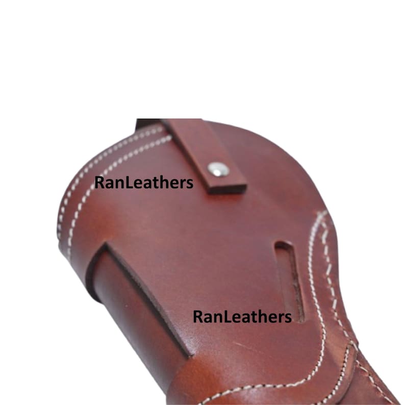 Może przedstawiać: Brązowa sk&oacute;rzana kabura z białymi przeszyciami i napisem "RanLeathers". Kabura posiada pasek z zapięciem na srebrny guzik. Sk&oacute;ra ma bogaty, ciemnobrązowy kolor.