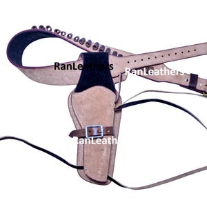 Puede incluir: Una funda de cuero marrón con un cinturón a juego y bucles para balas. La funda tiene un acento de gamuza negra y una hebilla plateada. El cinturón es marrón con una hebilla dorada. La imagen es de un cinturón y funda de pistola de estilo occidental.