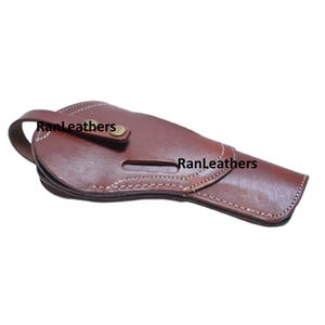 Może przedstawiać: Brązowa sk&oacute;rzana kabura z białymi przeszyciami i napisem "RanLeathers". Kabura posiada pętlę na pasek i zapięcie na zatrzask. Kabura jest przeznaczona do przechowywania broni palnej.